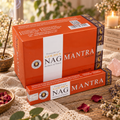 Confezioni arancioni di incenso Golden Nag Mantra, con un bastoncino acceso sullo sfondo.